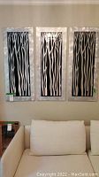 Full view of three matching rectangular wall art panels mounted above couch, showing silver frames and black and white tree branch pattern.