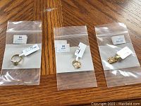 Three 10 kt gold items individually bagged on a wooden surface: butterfly charm, Nana heart charm, and baby ring.