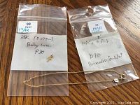 Photo showing two plastic bags, one containing a small 14 kt gold baby cross pendant and the other an 8-inch 14 kt gold bracelet/anklet chain laid out on a wooden surface.