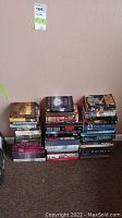 Three stacks of mixed hardcover and softcover books on floor against a beige wall.