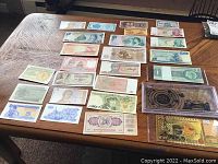 Overview of approximately 27 foreign currency bills laid out on a table displaying various colors, designs, and countries.