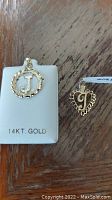 Top view photo of the two gold charms, one round 14kt gold charm with letter J, and one heart-shaped gold charm with letter P.