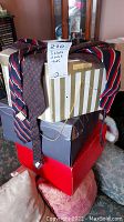 Photo showing ties draped over striped and polka-dot patterned hat boxes, with a handwritten note '210 3 hats 3 pairs ties'