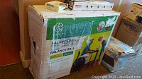 Boxed Gaiam Balance Ball Chair with visible label and packaging showing a person sitting on the ball chair at a desk.