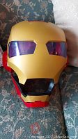 Front view of Iron Man helmet showing red and gold colors, with purple-tinted eyes and open mouth area.