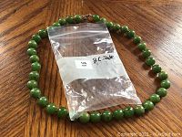 Full view of the round green B.C. jade bead necklace with plastic bag labeled 'B.C. Jade'.