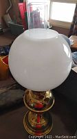 Full view of the brass oil lamp with white globe and clear chimney, showing overall shape and size.