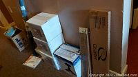 Boxes and items in hallway including three white boxes of wall lamps, a boxed strip lamp labeled Quartz, and other repair items