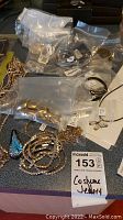 Multiple pieces of costume jewelry including necklaces and bracelets displayed on a table with identification tag '153'