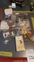 Photo of assorted costume jewelry including rings, brooches, earrings, and pins displayed on a dark surface. Some items are in branded plastic bags and boxes.