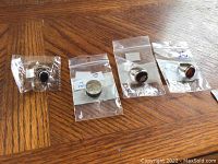 Four sterling silver rings in clear bags on wooden surface, marked 925 with semi-precious stones in varied colors and shapes.