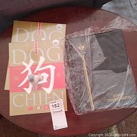Two Year of the Dog stamp books with a beige and pink cover showing a dog image and Chinese character along with a dark brown stamp drying book with gold lettering and emblem.