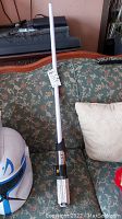 Full view of the light saber standing upright on a patterned sofa, showing the white blade and handle details.