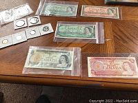 Overview of vintage Canadian coins and banknotes including $1 and $2 bills in protective sleeves.