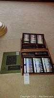 Wooden case with three trays displayed containing paint tubes and colored pencils, with Canson Bristol paper pad placed beside it.