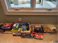 Photo showing the full group of board games and puzzles on the floor under window lighting including Risk & Castle Risk, Clue, Upwords, Blokus, and others.