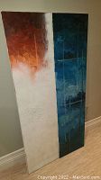 Full view of two abstract canvas panels leaning against a wall showing warm red/orange/white tones on one panel and cool dark blue tones on the other.