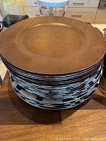 Stack of multiple decorative chargers shown from top revealing brown smooth surfaces.