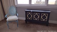 Full shot showing the metal chair with painted design and the black wooden credenza with patterned cupboard doors.