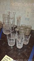All sixteen pieces of crystal including Waterford, showing jugs, glasses and candle holders arranged on a kitchen counter.