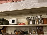 Two shelves with a rolled sleeping bag, white Ceratech electric heater, several metal pitchers and vases with different shapes and finishes, and a brown vase.
