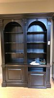 Front view of entire black painted bookcase showing two arched shelving compartments and lower cabinet
