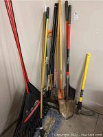 Full view of the garden tools including rakes, shovels, hoes, mop, gloves.