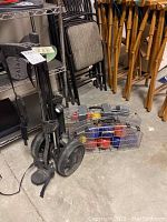 Golf rolling cart with wheels and carrying strap, standing upright next to bocce ball set in metal rack on floor