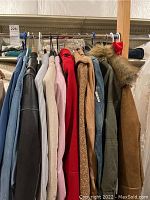 Photo showing a variety of women's jackets and outerwear hanging on a rack with different colors and materials.