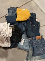 Photo showing a pile of twelve pairs of jeans with varied colors and styles.