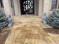 Two grey metal guardian statues flanking a front door on tiled patio, showing overall composition and scale