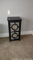 Front view of black wooden cabinet with mirrored front door featuring circular design patterns.