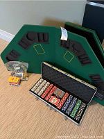 Wide view of poker chips in metal case, green felt table cover with chip holders, and bag with poker accessories on carpeted floor.