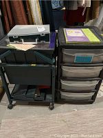 Two black plastic storage shelves on floor holding craft supplies