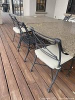 Six chairs arranged around outdoor stone table on wood deck, four with cushions