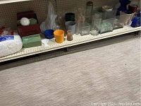 Shelf with various clear glass vases, floral foam blocks, and small containers in different colors and materials.