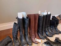 Photo showing six pairs of women's boots lined up, including black leather, brown leather, and black rubber boots.