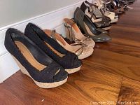View showing multiple pairs of women's shoes lined up including black wedge heels and several strappy sandals and high heels in various neutral tones.