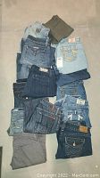 Pile of over a dozen pair of women's size 29 jeans of mixed washes and colors including blue, dark denim, grey, and olive