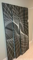 Full view of four joined wood panels with abstract white linear pattern on black background forming a mural, leaning against wall