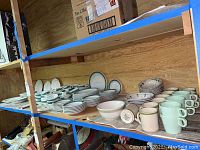Multiple shelves with assorted white and cream stoneware plates, bowls, cups, and mugs arranged on wooden shelving.