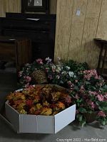 Photo showing faux pink and white flowers with green leaves and an attached woven basket, also includes a fall leaf wreath inside a white box.