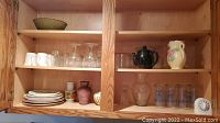 Wooden cabinets with various glassware including white Mason jar glasses, etched water glasses, decorative bowls, teapot, vases, plates, and timer