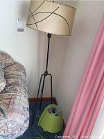 Floor lamp with beige drum shade and black tripod metal base near sofa