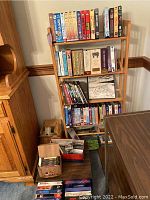 Full view of wooden media rack filled with VHS tapes, DVDs, cassettes in boxes on the floor and shelf, showing organizational setup and quantity.