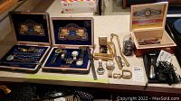 Overview of watches in display cases, tie clips, cufflinks, grooming kit, cigar boxes, belt buckles and other accessories on table