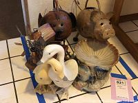 Photo shows a collection of animal figures including ducks, two hollow metal pigs, a fish-themed shell-shaped figure, and a barn with metal windmill blades on a tiled surface.