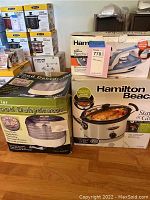 Photo showing boxed Hamilton Beach Stay or Go slow cooker crockpot, Hamilton Beach iron box, and 5 Tier Food Dehydrator box