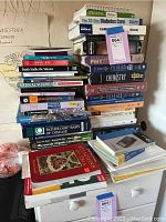 Stack of medical, health, and science textbooks and reference books piled on furniture with a map visible in background.