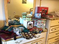 Two ceramic Christmas mugs, boxed simmer pot and salt & pepper shakers, decorative plates, and Christmas themed cloth items on dresser